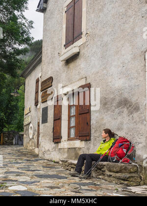 Donna escursionista tenendo il resto su una banca di fronte a un vecchio edificio nel villaggio di Gavarnie, Francia Foto Stock