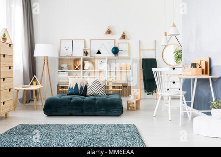 Cuscini modellato su futon verde in un accogliente salotto interno con sedia bianca al banco sotto lampade Foto Stock