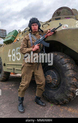 Un soffice come l'aria giocatore indossa Tedesco orientale, Junior Non-Commissioned ufficiali uniforme con un AK-47 si fermò un BDRM sovietica veicolo blindato Foto Stock