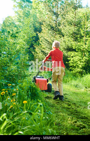 Bambino ragazzo aiutando nel giardino la falciatura di prato con un tosaerba Foto Stock