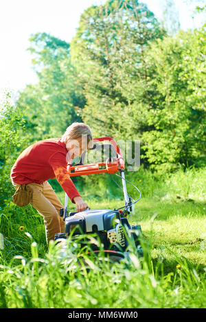 Bambino ragazzo aiutando nel giardino la falciatura di prato con un tosaerba Foto Stock