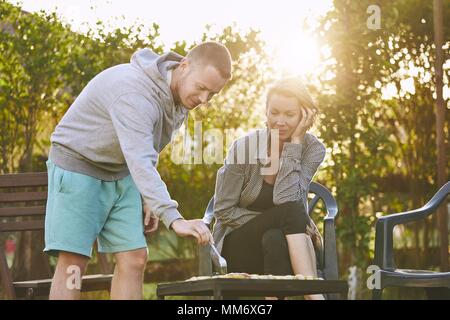 Estate in giardino. Coppia giovane alla brace contro chalet al tramonto. Foto Stock