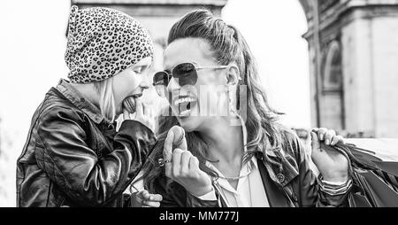 Elegante autunno a Parigi. Felice giovane madre e figlia con borse per lo shopping in Parigi, Francia mangiare amaretti Foto Stock