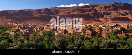 Foto panoramica della città di Tinghir, una striscia di case su un lussuoso verde foresta di palme sul pendio di una montagna rossa, Marocco orientale. Foto Stock