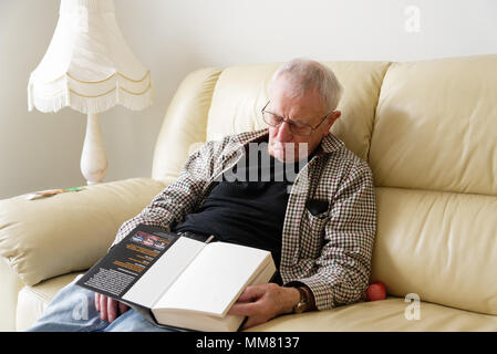 Anolder uomo addormentato sul divano mentre la lettura di un libro Foto Stock