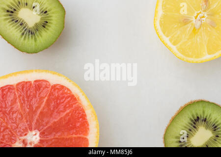 Fette di Ripe Juicy Limone pompelmo Kiwi in marmo bianco sullo sfondo di pietra. Uno stile di vita sano vitamine pulire il concetto di mangiare. Cornice piana copia laici Spac Foto Stock