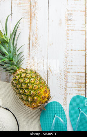 Piatto disposizione laici composizione con Frutti Tropicali ananas donne Hat pantofole blu su bianco Planked Sfondo legno. Vacanza Viaggiare Relaxatio Foto Stock