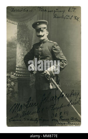Antico tedesco foto del 1919: un uomo in uniforme con un baffi neri e una spada sulla sua cintura. L'attore di teatro. Autografo. Allestimento militare. Foto Stock
