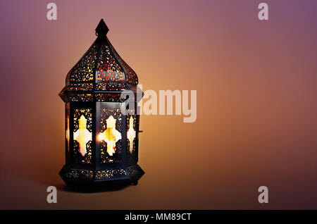 Ornamentali marocchino scuro, arabo lanterna sul tavolo. Candela che brucia nella notte. Biglietto di auguri per la comunità musulmana sacro mese del Ramadan Kareem. Festive sfondo sfocato. Foto Stock