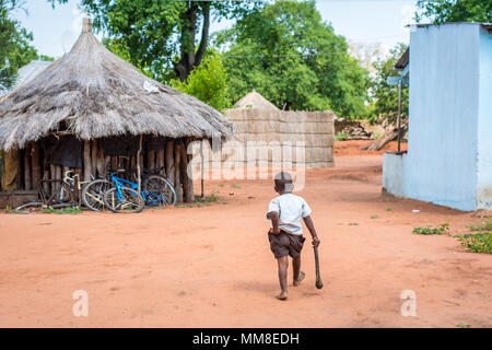 Giovani zambiani boy passeggiate lontano attraverso il villaggio tenendo una mano sul ascia di guerra e i suoi pantaloni, Mukuni Village, Zambia Foto Stock