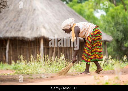 Donna dello Zambia nel tradizionale mantello modellato a mano usa scopa per spazzare fino lettiera che è stato gettato sulla terra, villaggio Mukuni, Zambia Foto Stock