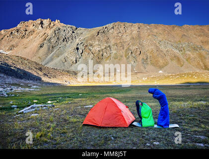 Divertente rilassante turistica in sacchi a pelo vicino a Orange in tenda sulle montagne di sunrise Foto Stock