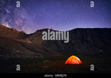 Tenda arancione si accende sotto il cielo notturno pieno di stelle e la Via Lattea in montagna in Kazakistan Foto Stock