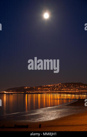 Luna piena riflettendo in mare nel corso di Colwyn Bay beach di notte, costa del Galles Settentrionale Foto Stock