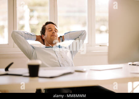 Imprenditore in un momento di relax a casa seduti davanti al suo tavolo di lavoro. L'uomo prendendo una pausa e ascoltare la musica tramite auricolari con gli occhi chiusi. Foto Stock