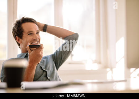 Uomo con un cellulare in mano e parlando su altoparlante guardando lontano. Imprenditore lavorando comodamente da casa sua. Foto Stock