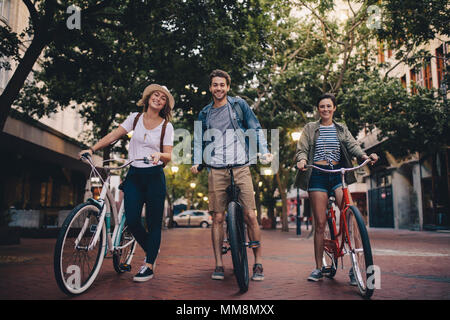 Lunghezza completa di tre giovani con le loro biciclette su strada della citta'. Amici sulla corsa in bicicletta attraverso la città. Foto Stock