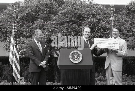 Ronald Reagan (1911–2004) è stato il 40° presidente degli Stati Uniti d'America, dal 1981 al 1989 e in precedenza governatore della California e attore cinematografico. L'immagine d'archivio registra la partecipazione di Reagan a una presentazione cerimoniale che coinvolge un assegno a fianco dei rappresentanti dell'agenzia, documentando un evento formale governativo o istituzionale conservato come una stampa fotografica storica. Foto Stock
