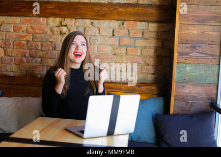 Bella ragazza fortunato godendo di vincere le scommesse online dal computer portatile presso il cafe. Foto Stock