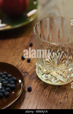 Un bicchiere di gin con bacche di ginepro (Juniperus communis) su un tavolo rustico Foto Stock