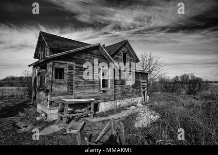 Foto in bianco e nero di un vecchio scary abbandonato farm house che peggiora con il tempo e l'incuria. Foto Stock