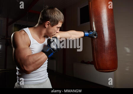 Giovane maschio muscolare boxer punch sacco da boxe in palestra interno Foto Stock