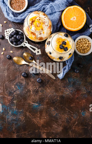 In casa sano dessert stratificata scherzare con Orange, mirtillo, biscotti, yogurt e granola in bicchieri. Vista dall'alto. Posto per il testo Foto Stock