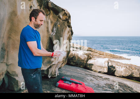 Giovane scalatore rivestimento uomo le mani in gesso in polvere di magnesio per arrampicata a la costa Foto Stock