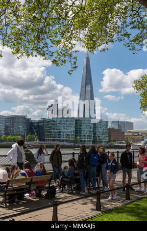 Un gruppo di turisti raccolti sulla sponda nord del fiume Tamigi vicino alla Torre di Londra con la shard edificio per uffici in background Foto Stock