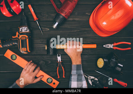 Vista parziale del lavoratore mantenendo la livella e martello con diverse alimentazioni intorno sulla superficie di legno Foto Stock