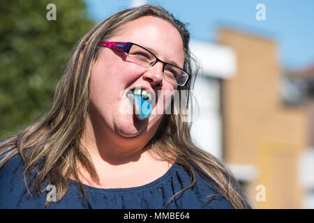 Donna con la lingua fuori dopo aver bevuto blu cucciolo slush drink, mostrando le macchie blu sulla sua lingua e denti, mentre sorridente in estate. Felice concetto. Foto Stock