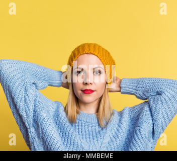 Ritratto di una giovane donna bellissima con un cappello di lana in studio su sfondo giallo. Foto Stock