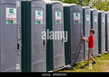 Fila di servizi igienici portatili con porta di apertura ragazzo per entrare in uno al Hampshire Game & Country Fair, Netley Marsh, Hampshire UK a maggio