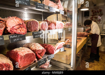 In prossimità di vari tagli di manzo su scaffali in una macelleria, uomo che indossa il grembiule permanente al macellaio blocco. Foto Stock