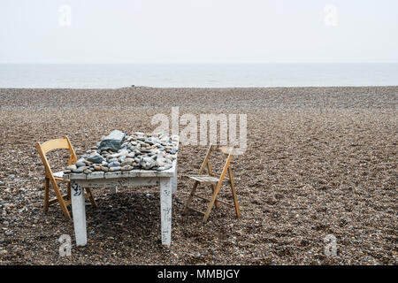 Vecchio traballanti di legno bianco etichetta coperta in ciottoli e due sedie pieghevoli su una spiaggia di ciottoli dall'oceano. Foto Stock