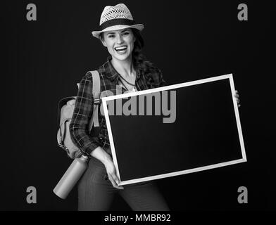 La ricerca di luoghi ispiratrice. sorridente donna attiva escursionista in un plaid shirt mostra blank board sullo sfondo Foto Stock