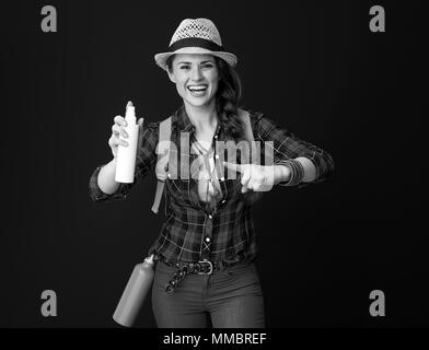 La ricerca di luoghi ispiratrice. Sorridendo turistica attiva donna con zaino rivolti a un flacone spray isolato su sfondo Foto Stock