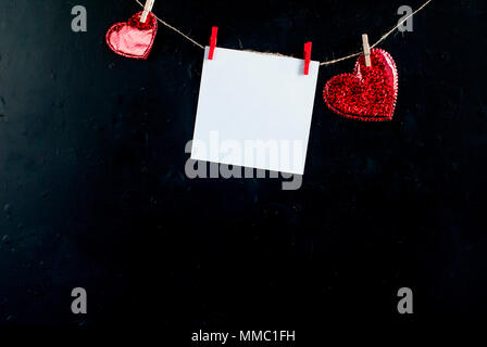 Foglio per note e cuori pinned mollette ad una fune su uno sfondo nero Valentins giorno spazio di copia Foto Stock