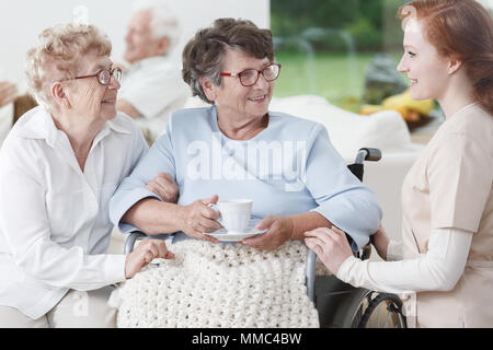 Infermiere e le donne anziane hanno divertimento durante la conversazione nella sala comune Foto Stock