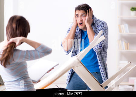 Moglie aiutando il marito per riparare sedia rotta a casa Foto Stock