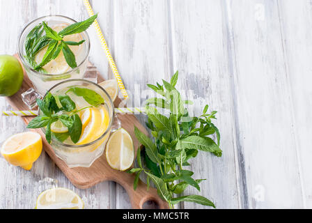 Freschi Fatti in casa la limonata nel bicchiere con ghiaccio e menta, gli ingredienti dei cocktail, limone e fettine di lime e foglie di menta bianca sul tavolo di legno, spazio di copia Foto Stock