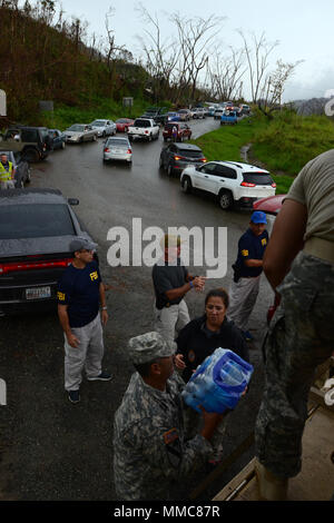 Gli agenti FBI e U.S. Esercito di soldati di riserva da 393 contro il supporto del battaglione di supporto, 166a sostegno regionale, gruppo 1a sostegno della missione il comando, acqua di scarico in Adjuntas, Puerto Rico, 11 ott. 2017, come residenti linea la strada per ricevere la merce. Le agenzie governative unito gli sforzi per fornire aiuto in caso di catastrofe in Puerto Rico dopo l uragano Maria ha causato danni catastrofici. (U.S. Foto dell'esercito da Staff Sgt. Elvis) Foto Stock