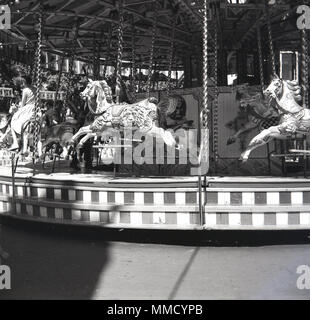 Anni sessanta, storico, giovane ragazza in sella ad un cavallo di legno su di una giostra o merry-go-round alla fiera del divertimento al parco di Battersea, Londra, Inghilterra, Regno Unito. La fiera è stata costruita per il 1951 Festival di Bretagna celebrazioni nella sezione settentrionale del parco ed è stata una delle principali attrazioni per molti anni. Foto Stock