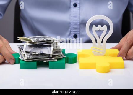 Mano umana tenendo il giallo e il verde Puzzle con lampadina elettrica e delle banconote in euro Foto Stock