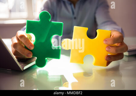 Close-up di commercianti la mano che regge due White Jigsaw Puzzle su scrivania Foto Stock