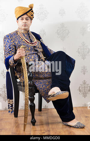 Uno di Rajasthani Royal -Groom Sittng sedia stile Sherwani nozze con la spada Foto Stock