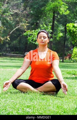 Una donna seduta Fitness erba fare yoga Padmasana meditazione In-Park Foto Stock