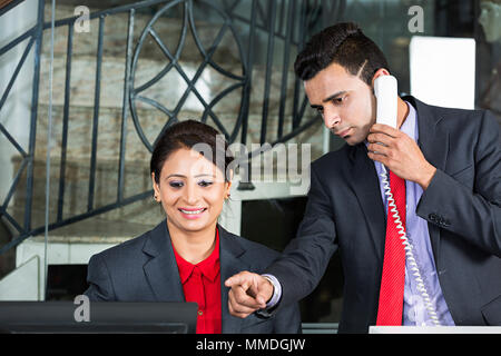 Due Receptionist s dipendente parlando di puntamento Telefono Laptop-Screen Hotel CONTATORE DI RICEZIONE Foto Stock