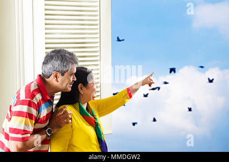 Felice coppia Senior cercando-fuori una finestra che mostra di puntamento a domicilio degli uccelli Foto Stock