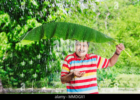 Felice l'uomo Senior Banana-Leaf sotto la pioggia battente.In mani Fun-Cheerful Garden Foto Stock